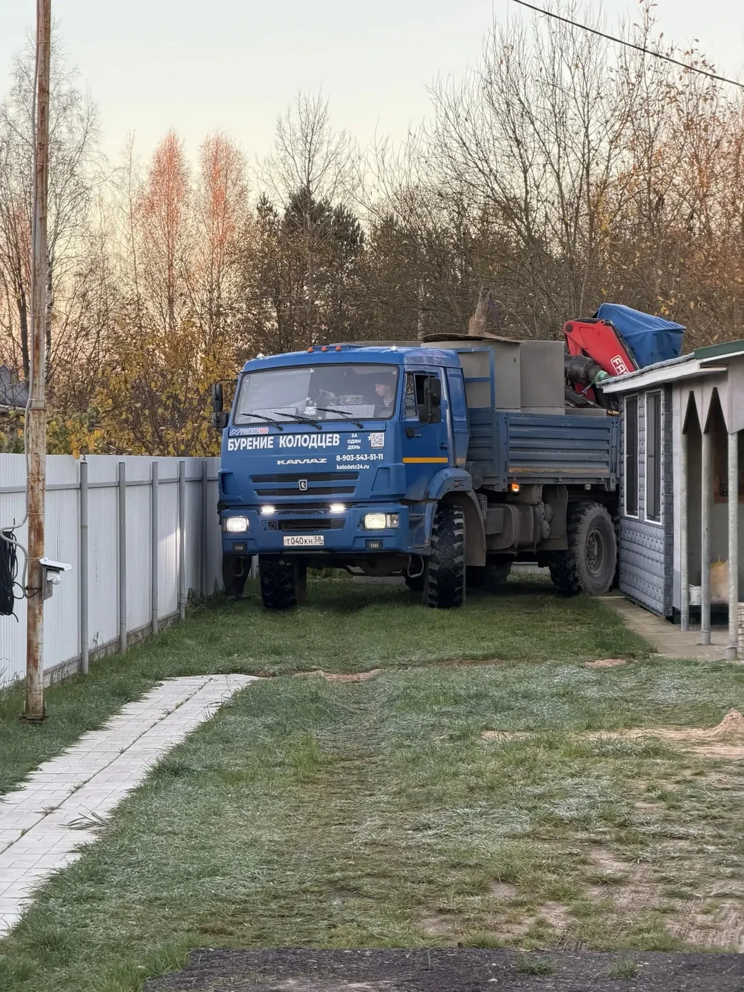 КамАЗ с надписью «Бурение колодцев» на борту стоит у ворот участка