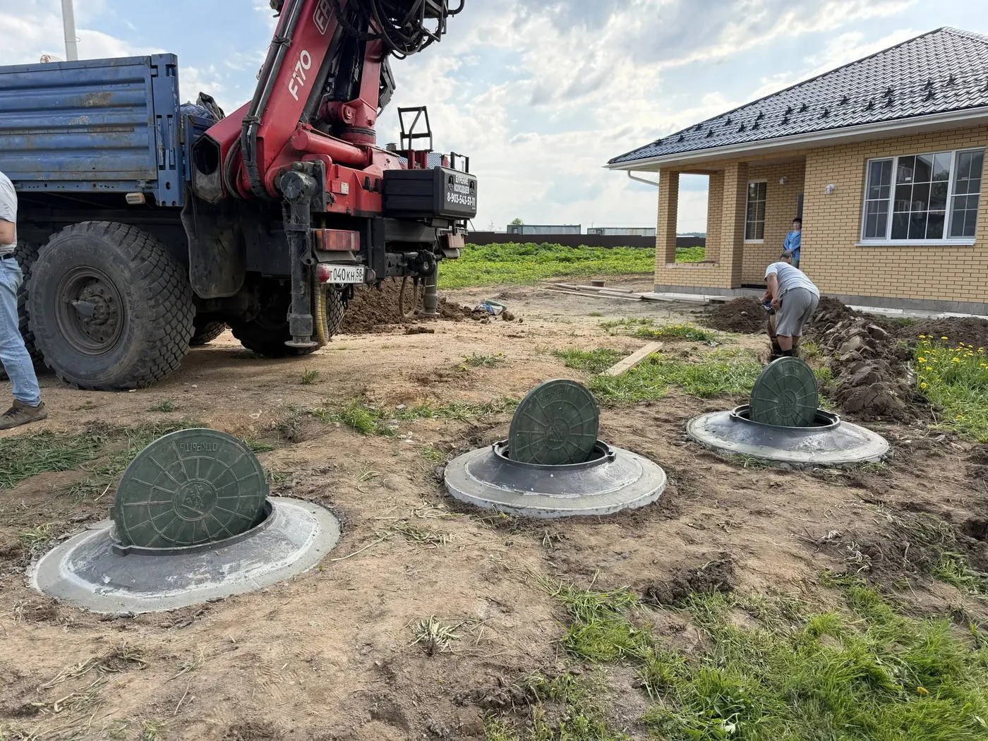 Три люка септика из колец у нового дома, рядом КамАЗ с манипулятором